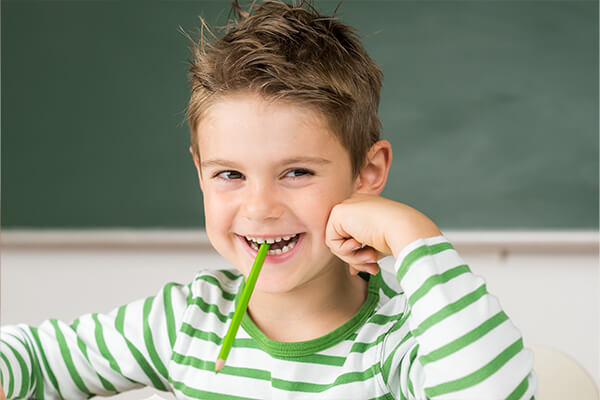 Lächelndes Kind mit Stift im Mund Artikel Kieferorthopädie Hamburg